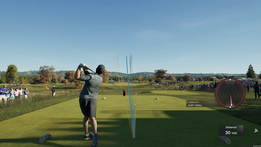 Golfista odpaľuje na sviežom, slnkom zaliatom ihrisku, diváci v jeho blízkosti. Grafy a merač vzdialenosti prekrývajú obraz, čo naznačuje, že sa jedná o videohru.