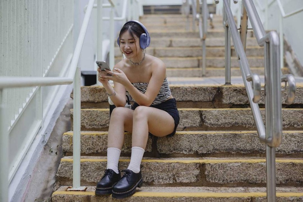 Slúchadlá JBL Tune 730BT fialová Žena sediaca na schodoch používa bezdrôtové slúchadlá JBL Tune 730BT pri počúvaní hudby zo smartfónu