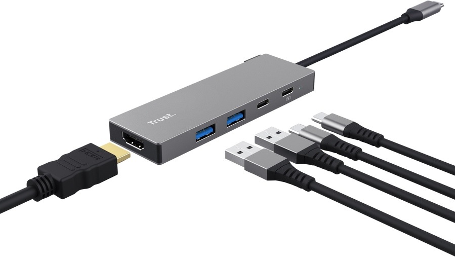 USB Hub Trust DALYX 5v1 strieborný Na obrázku je strieborný USB-C hub Trust DALYX 5v1 zobrazený pri použití s viacerými káblami. Z pravej strany z neho vedie pevný kábel zakončený USB-C konektorom na pripojenie k notebooku. Na tele hubu sú vidieť dva modré USB porty, dva menšie USB-C porty a na čele HDMI konektor, do ktorého je zapojený HDMI kábel. Vedľa hubu ležia ešte ďalšie USB a USB-C káble, takže obrázok zdôrazňuje možnosti pripojenia viacerých zariadení naraz.