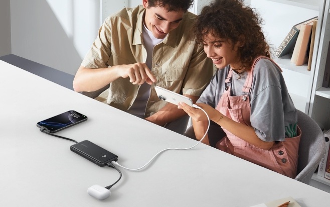 Muž a žena sledujú obrazovku smartfónu pripojeného k powerbanke Anker Zolo spoločne s ďalším telefónom a slúchadlami