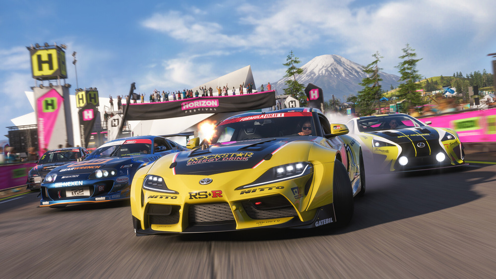 Závodná hra Forza Horizon 6 so záberom na horské prostredie s tromi športovými vozidlami v akcii. Živý dav a transparenty vytvárajú vzrušujúcu a dynamickú atmosféru.