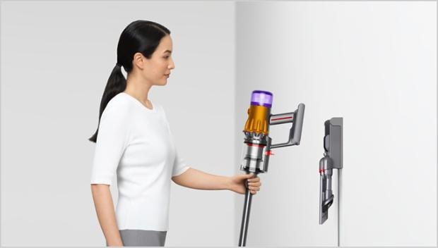 Tyčový vysávač Dyson V12 Detect Slim Absolute 2026 strieborný Pani dáva tyčový vysávač Dyson V12 Detect Slim Absolute po upratovaní do nástenného držiaka, kde bude pripravený a vždy po ruke.