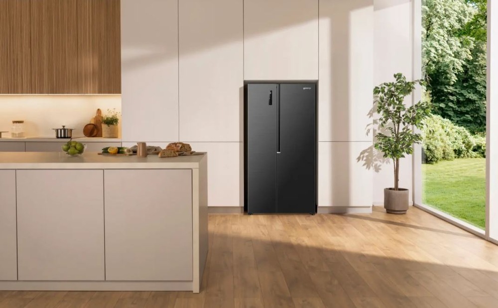 Americká chladnička Gorenje G400 NRS917D41BX čierna čierna americká chladnička Gorenje NRS917D41BX umiestnená vo svetle kuchyni vedľa záhrady, ktorá je vidieť cez presklenú stenu.