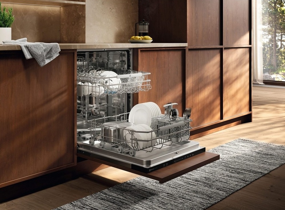 Umývačka riadu Electrolux Série 600 E62LB100S Otvorená umývačka Electrolux plná čistého riadu. Koše sú ľahko vysunuté. Umývačka je v kuchyni s dreveným dekorom.