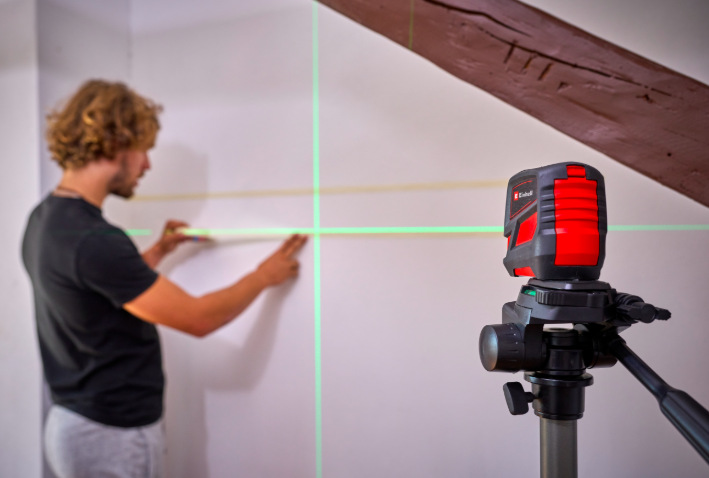Krížový laser Einhell TCLL2G Muž používa krížový laser Einhell TCLL2G na statíve pri zarovnaní poličky na stene