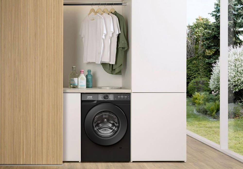 Práčka Gorenje G400 WG484A31B UltraClean čierna práčka Gorenje WG484A31B UltraClean medzi dvoma veľkými skriňami, nad práčkou visi tričká na ramienku