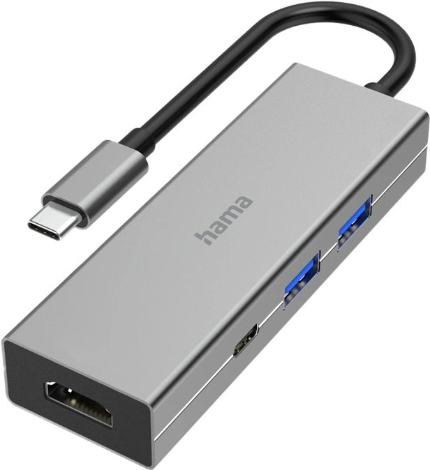 Na obrázku je šedý USB-C hub Hama Multiport zachytený šikmo spredu. Má úzke kovové telo s jednoduchým hranatým dizajnom a z jedného konca z neho vedie krátky čierny kábel zakončený USB-C konektorom. Na ľavom čele je HDMI konektor, na boku dva modro označené USB porty a jeden menší USB-C port. Na hornej strane je logo hama. Zariadenie pôsobí elegantne, kompaktne a je určené na rozšírenie konektivity notebooku alebo tabletu.