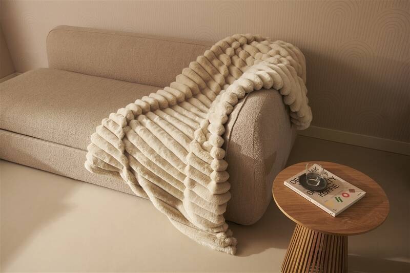 Vyhrievacia deka Duux DXOB01 Yentl Cuddle 200 x 200 cm béžová Béžová deka Duux Yentl prehodená cez látkovú pohovku v minimalistickom interiéri, vedľa drevený konferenčný stolík s časopisom, deka pôsobí nadýchane a hreje aj ako dizajnový doplnok.