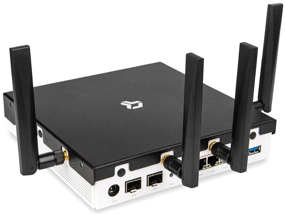 Router CZ.NIC Turris Omnia NG Wi-Fi 7 čierny Na obrázku je router Turris Omnia NG Wi-Fi 7 zachytený šikmo zozadu. Má ploché čierne telo s bielou spodnou časťou a štyri vysoké externé antény, dve po stranách a dve bližšie k stredu. Na zadnej strane sú vidieť konektory vrátane napájania, dvoch SFP portov, štyroch ethernetových portov a modrého USB portu.
