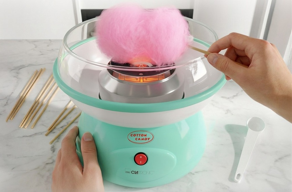 Výrobník cukrovej vaty Clatronic ZWM 3478 zelený Ruky navíjajúce ružovú cukrovú vatu na tyčinku v stroji Clatronic na mramorovom stole.