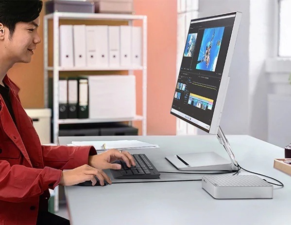 Muž pracujúci s fotografiami na monitore, ku ktorému je pripojený mini stolný počítač Lenovo IdeaCentre Mini