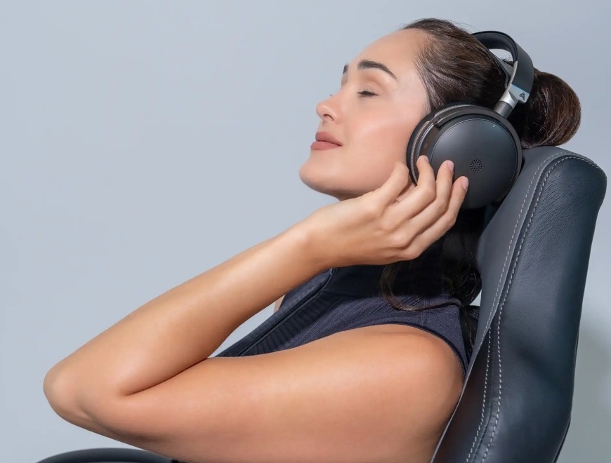 Headset Audeze Maxwell 2 ANC - PlayStation čierny Žena odpočívajúca v kresle s nasadeným headsetom Audeze Maxwell 2 ANC v lifestylovom zábere