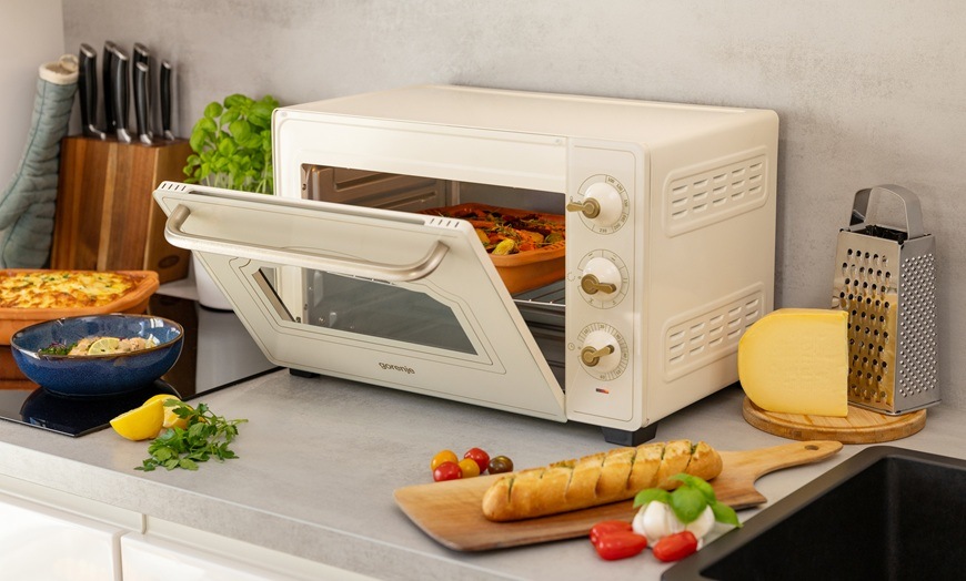 Mini rúra Gorenje Retro OM30CLI béžová Mini rúra Gorenje OM30CLI má pootvorené dvierka. Okolo nej sú rôzne pokrmy.