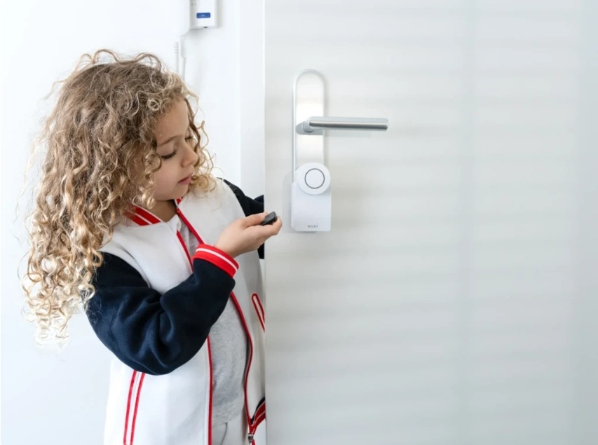 Dieťa otvárajúce dvere s Nuki Smart Lock pomocou diaľkového ovládača Nuki Fob.