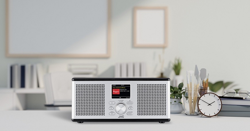 Moderné stereo rádio JVC RA-E775B-DAB s LCD displejom v bielom interiéri na pracovnom stole vedľa hodín a dekorácií