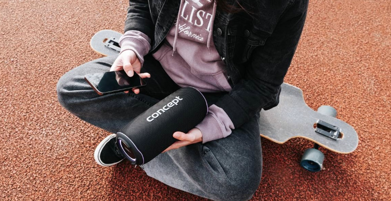 Osoba sediaca pri skateboarde drží reproduktor Concept SoundJoy BR5530 a ovláda hudbu telefónom