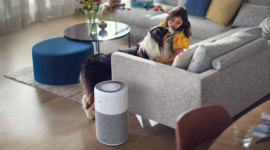Čistička vzduchu Philips AC2220/10 2000 Series vedľa pohovky, na ktorej sedí dievča hladiace si psa