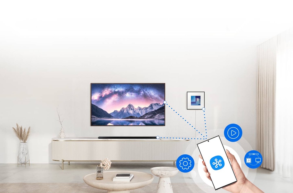Reproduktory Samsung HW-LS60D, Music Frame (2 ks) čierne Samsung HW-LS60D, Music Frame visí na stene obývacej izby vedľa televízii Samsung, pod ktorou na televíznom stolíku leží soundbar Samsung, v popredí ruka drží mobilný telefón, na ktorého displeji je logo aplikácie SmartThings, bodkované čiary spájajú mobil s TV, reproduktorom a soundbarom