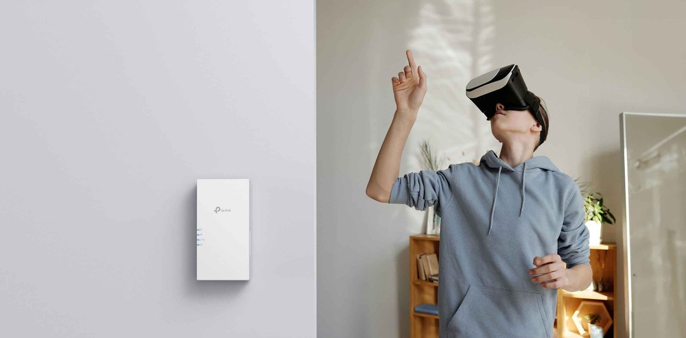 Osoba s nasadeným VR headsetom ukazuje prstom nahor v miestnosti s minimalistickým dizajnom. Na stene je namontovaný Wi-Fi extendér TP-Link.