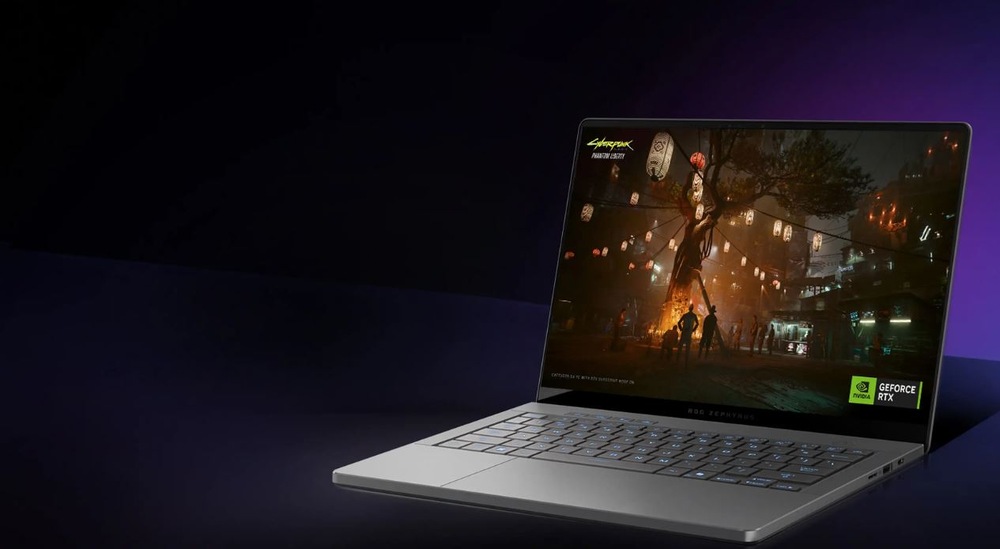 Elegantný šedý notebook otvorený na tmavom pozadí zobrazuje živú scemu mestskej panorámy hry Cyberpunk 2077.