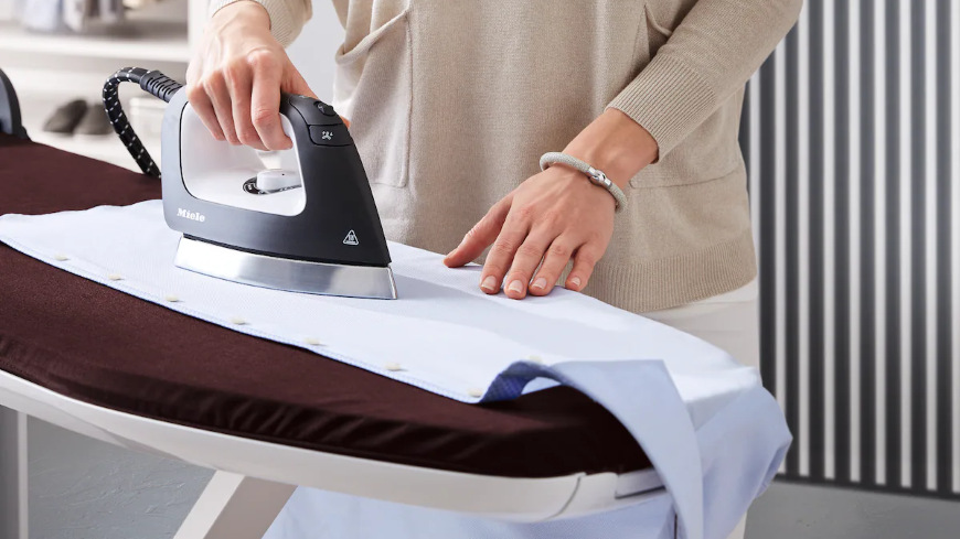 Žehliaci systém Miele B4847 FashionMaster 4.0 Žena žehlí košeľu na žehliacom systéme Miele B4847 FashionMaster 4.0″ width=