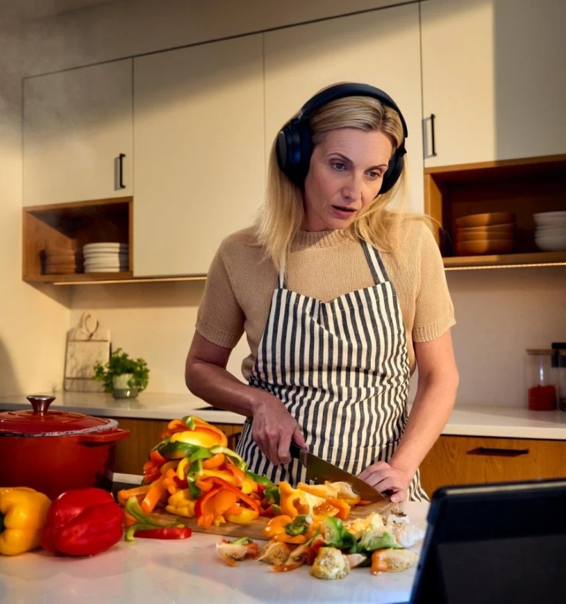 Slúchadlá Sennheiser RS275 TV čierna Žena krájajúca papriku sleduje video na tablete a má nasadené slúchadlá Sennheiser RS275 TV