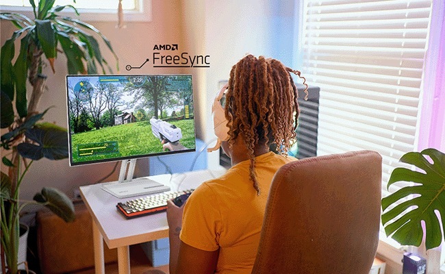 Monitor Lenovo L24-4C sivý Osoba sleduje videohru na monitore so zapnutou technológiou AMD FreeSync. Sedí v útulnej miestnosti s rastlinami a slnečným svetlom prúdiacim dovnútra.