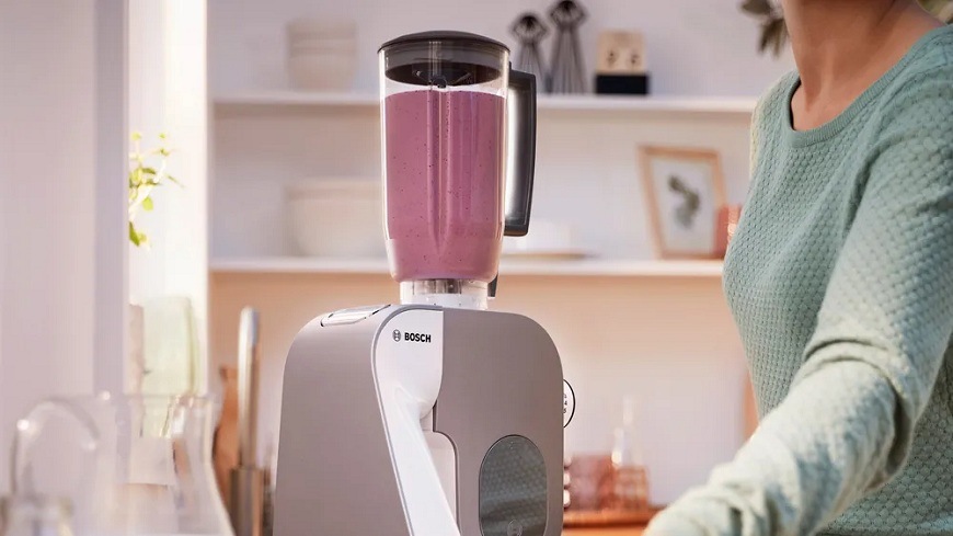 Kuchynský robot Bosch MUM 5 Scale MUM5XL74 biely/champagne Mixér naplnený kokteilom pripojený na kuchynský robot Bosch MUM5XL74, na pravej strane je vidieť časť ženskej postavy obsluhujúcej mixér