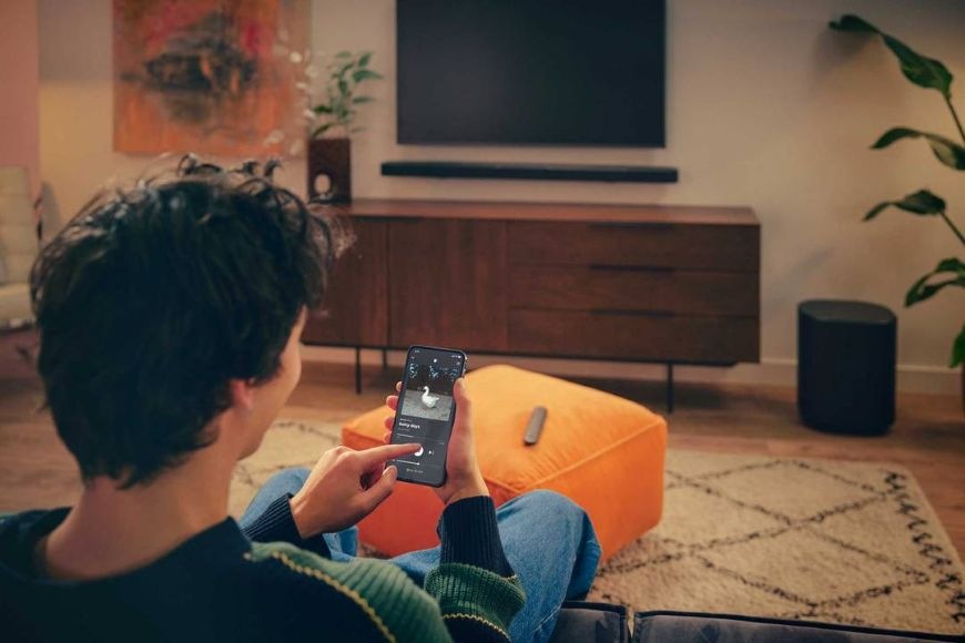 Muž streamuje hudbu do soundbaru JBL BAR 1000 MK2 pomocou telefónu