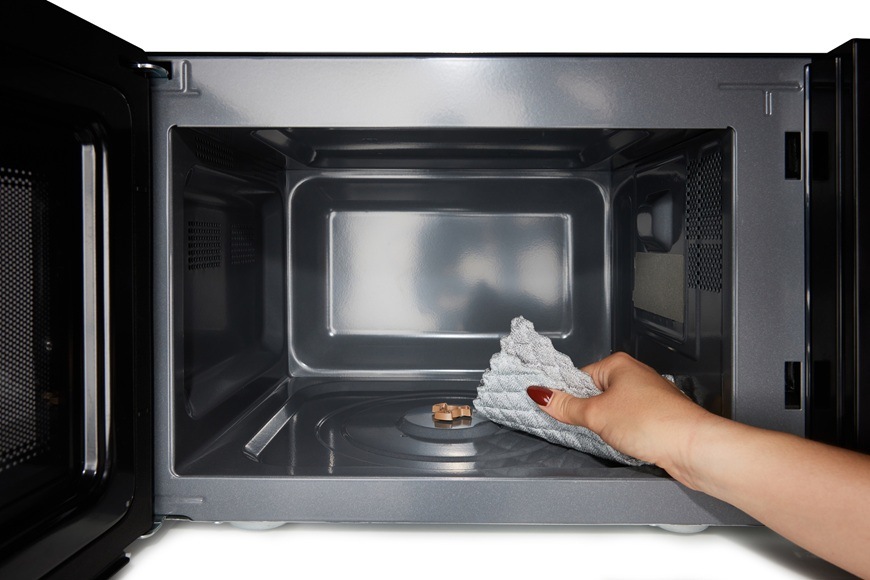 Mikrovlnná rúra Hisense H23MOBSD2H4 čierna Pohľad do otvorenej mikrovlnky Hisense H23MOBSD2H4. Pani stiera nečistoty navlhčenou handričkou.