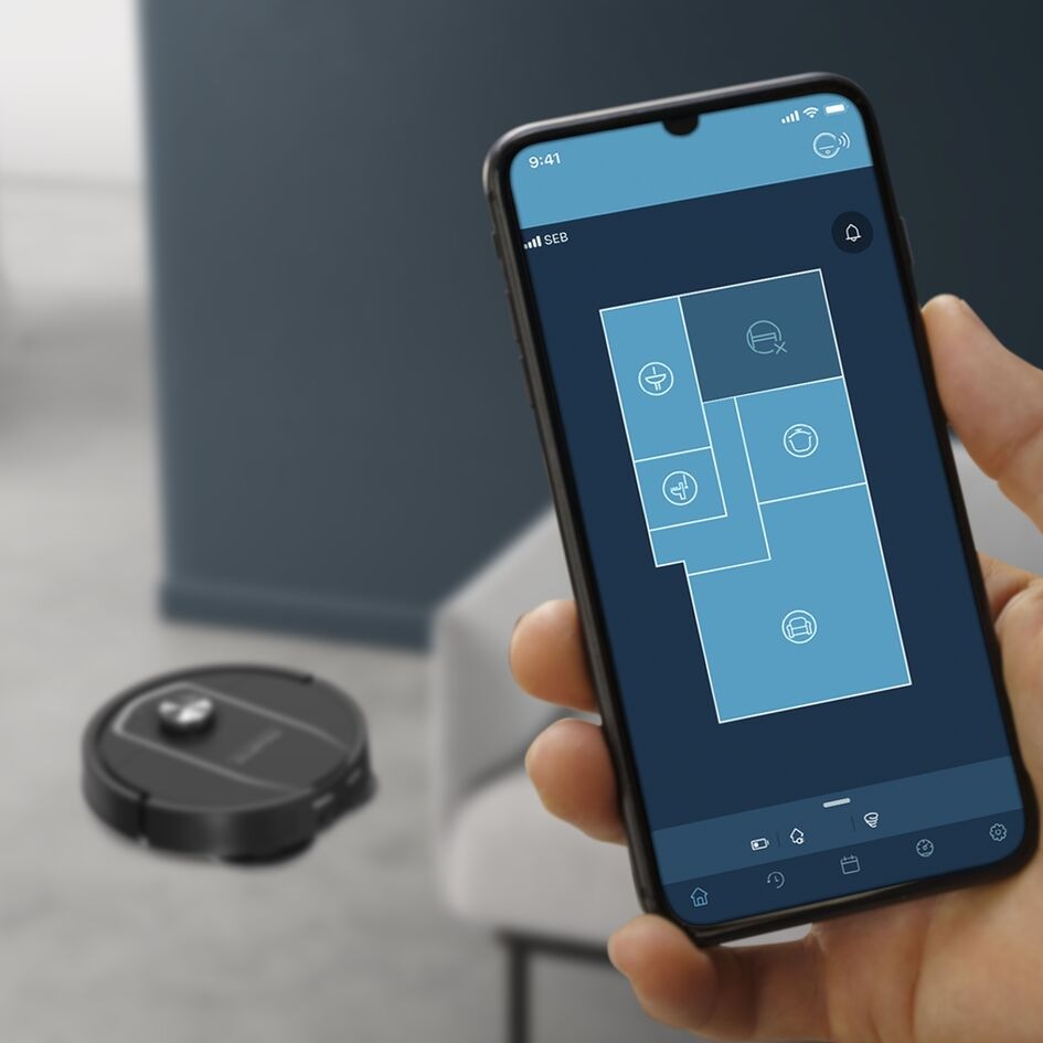 Robotický vysávač Rowenta X-Plorer S575 Max Wet & Dry 10000 PA RR95A5E0 čierny Ruka držiaca smarphone so zapnutou mobilnou aplikáciou Rowenta Robots a vysávač Rowenta RR95A5E0 na podlahe