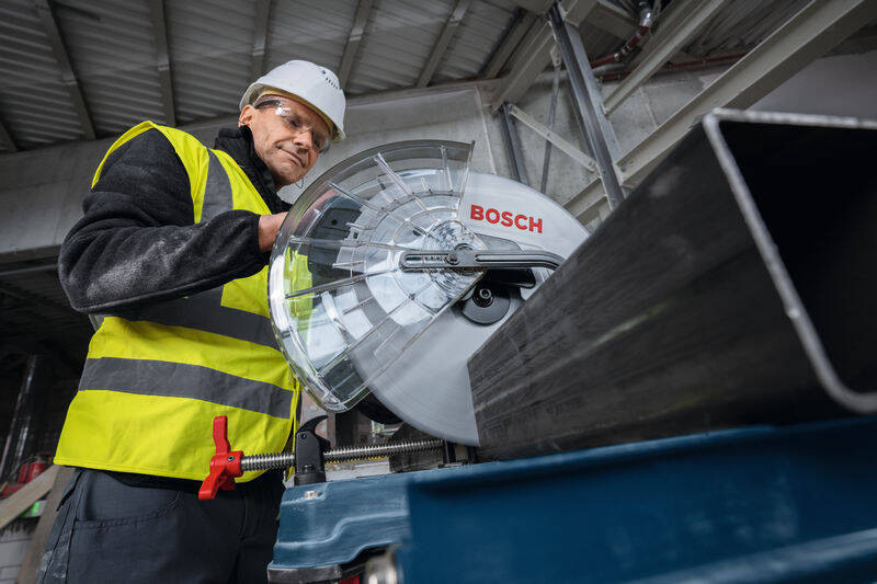 Píla na kov Bosch Professional GCD 18V-355 (bez baterie) Muž v ochranným pomôckam je zachytený pri rezaní kovového materiálu na píle Bosch Professional GCD 18V-355.