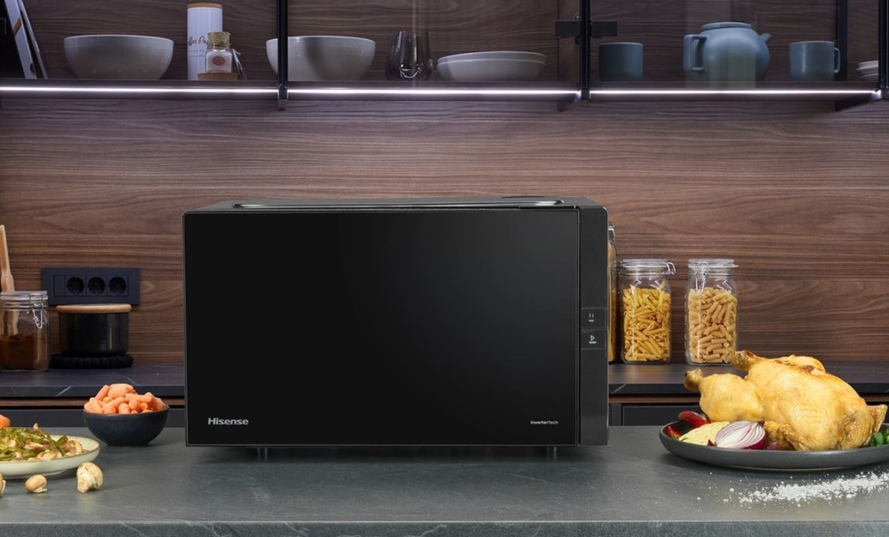 Mikrovlnná rúra Hisense H25MOBS4HGI Invertor čierna Mikrovlnná rúra Hisense H25MOBS4HGI na kuchynskej linke hnedej kuchyne. Vedľa sú taliere s jedlom