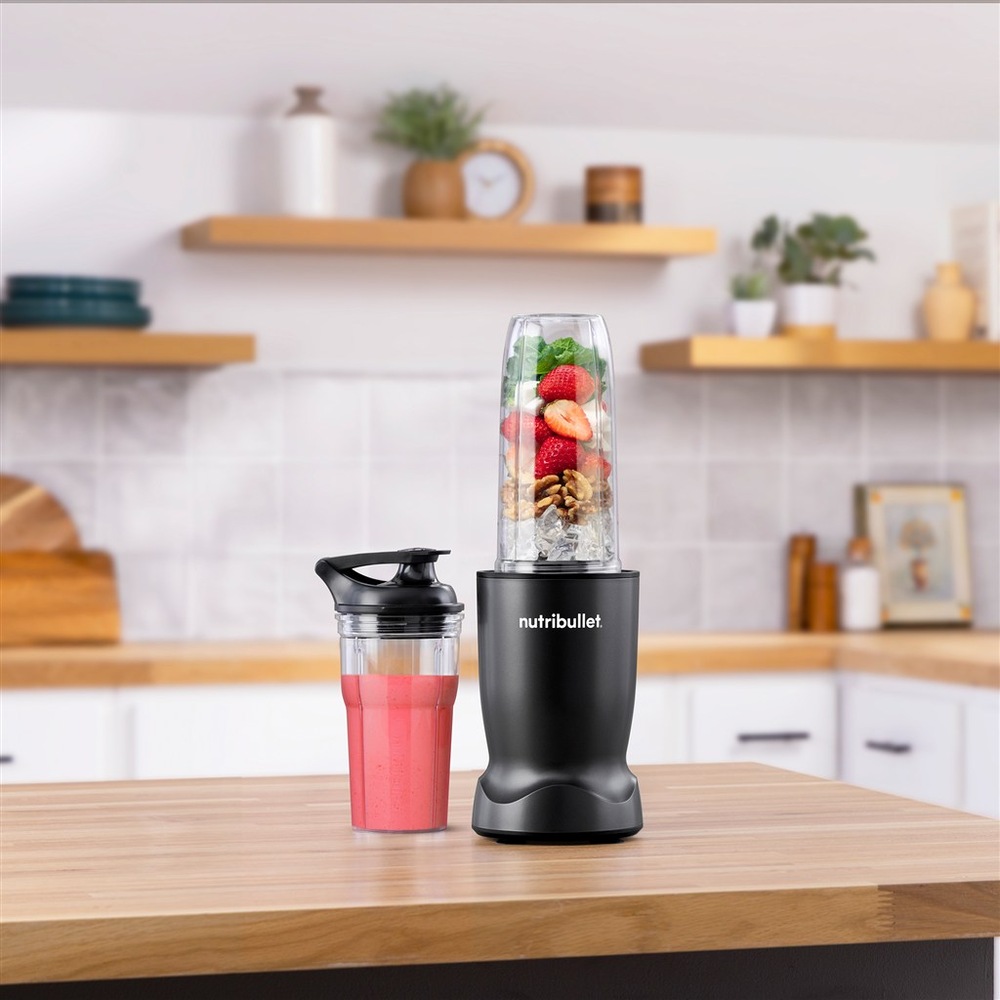 Stolný mixér Nutribullet TURBO 1000 NBT1006MB čierny Mixér NutriBullet na kuchynskom pulte vedľa prenosného téglika s ružovým smoothie.