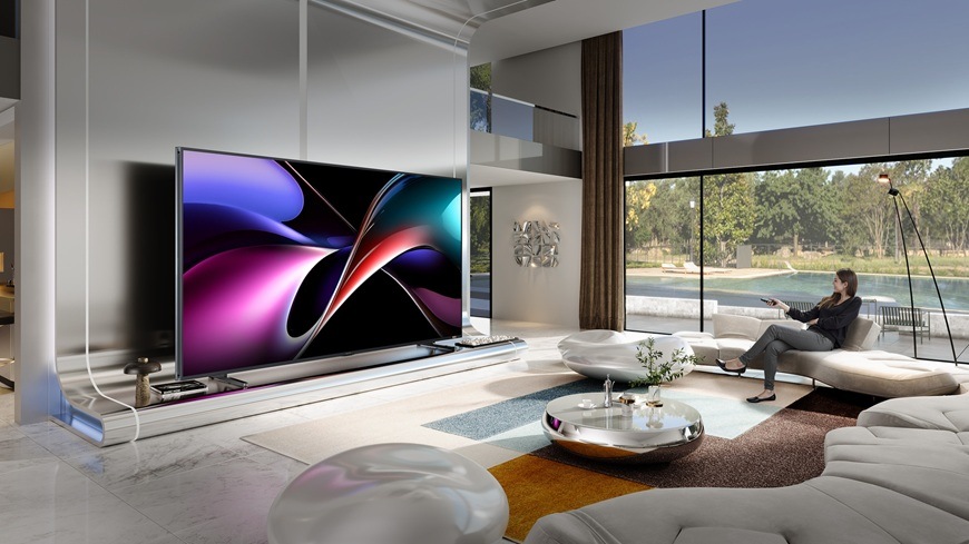 Na obrázku je žena, sediaca na gauči a zapína televízor Hisense 116UXQ pomocou diaľkového ovládača