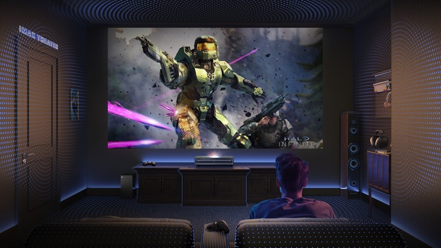 Muž sedí na gauči v domácom kino sále a pred sebou má zapnutý projektor Hisense PX3-PRO, na ktorom hrá akčnú hru.