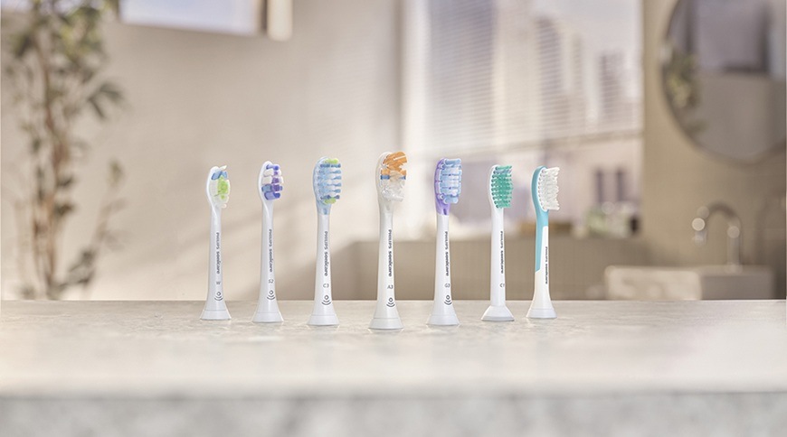 Rôzne náhradné hlavice pre elektrické zubné kefky Philips Sonicare usporiadané v rade na kúpeľňovej doske, každá s iným typom štetín.