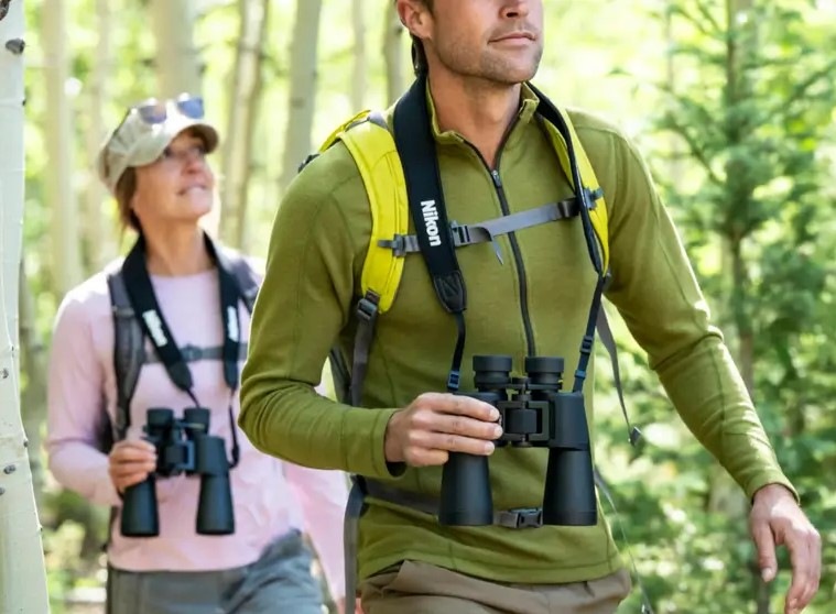 Muž so ženou idú lesom, každý má na krku ďalekohľad Nikon Action 16×50, ktorý zároveň drží jednou rukou.