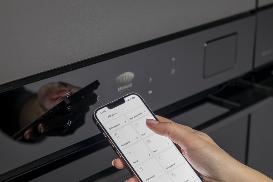 Žena v ruke drží šikovný mobilný telefón. V ňom má otvorenú aplikáciu ConnectLife pre diaľkové ovládanie rúry.