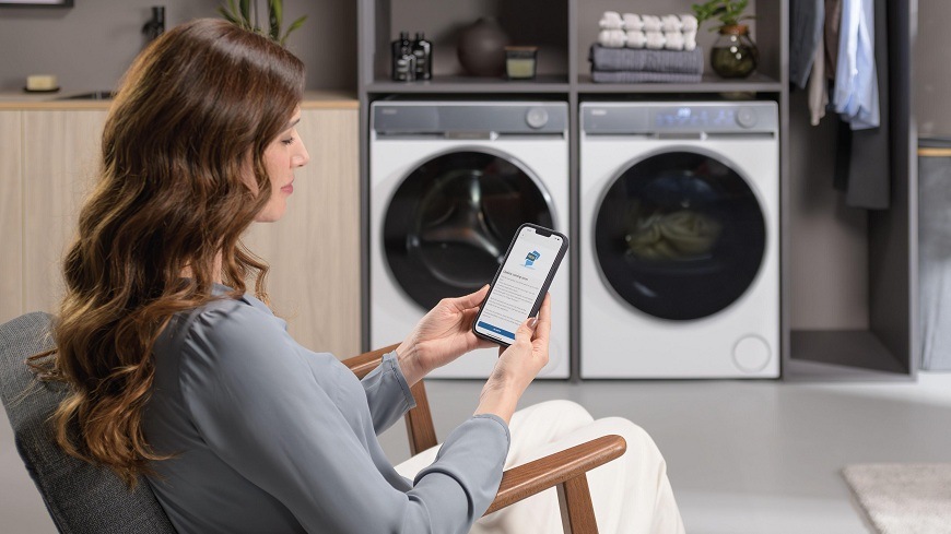 žena sa chystá k diaľkovému ovládaniu sušičky Haier HD90-AQ387U1-S a práčky haier pomocou mobilu a aplikácie hon