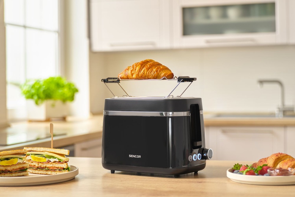 Hriankovač Sencor STS 2710BK čierny Croissant ohrievaný na mriežke hriankovača Sencor STS 2710BK, vedľa ktorého ležia hotové toasty a ďalšie raňajky.