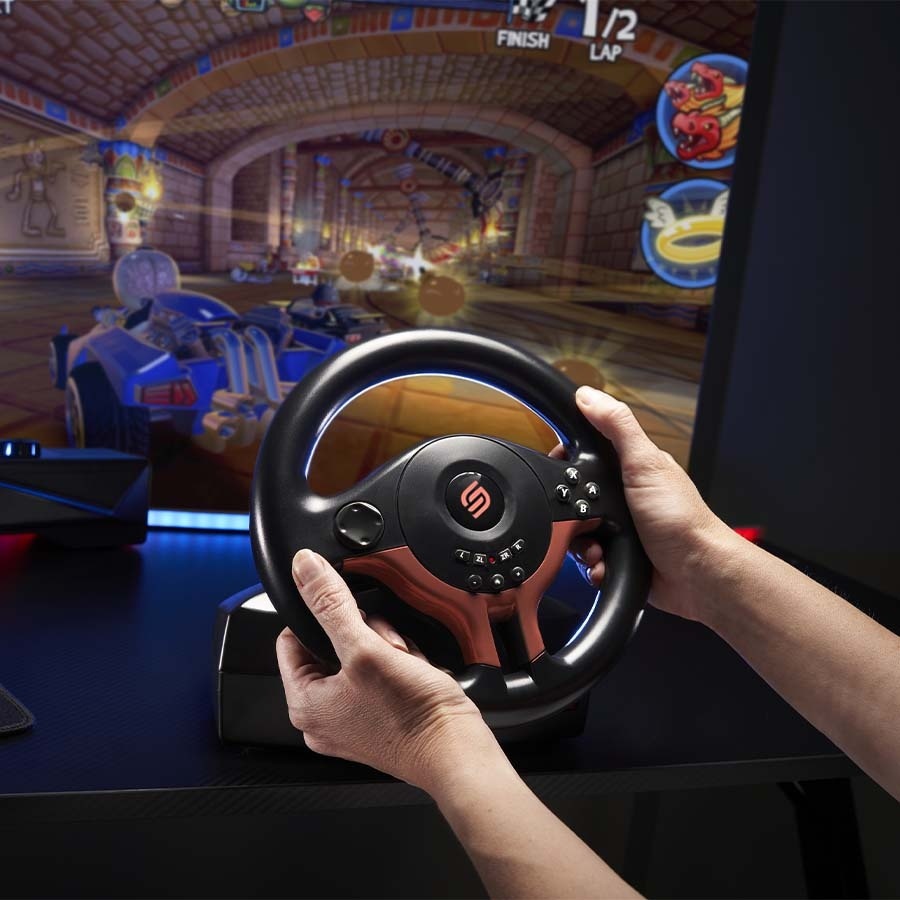 Volant SUPERDRIVE SV250 SP Edition Red červený Ruky zvierajúce herný volant pred záberom z hry Rocket League. Prostredie vyvoláva vzrušenie a ponorenie sa do deja.