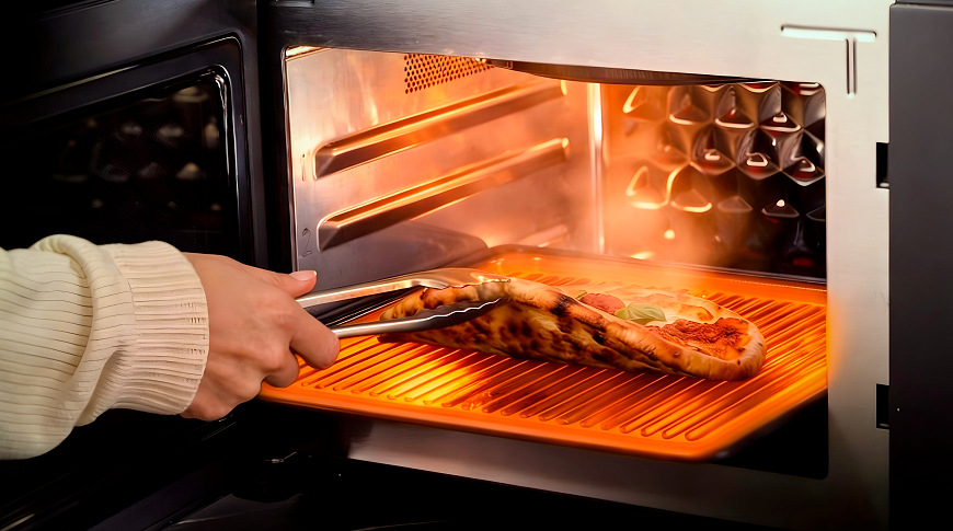 ruka vyťahuje pizzu z mikrovlnnej rúry a ukazuje, že je zospodu upečená dochrumkava.