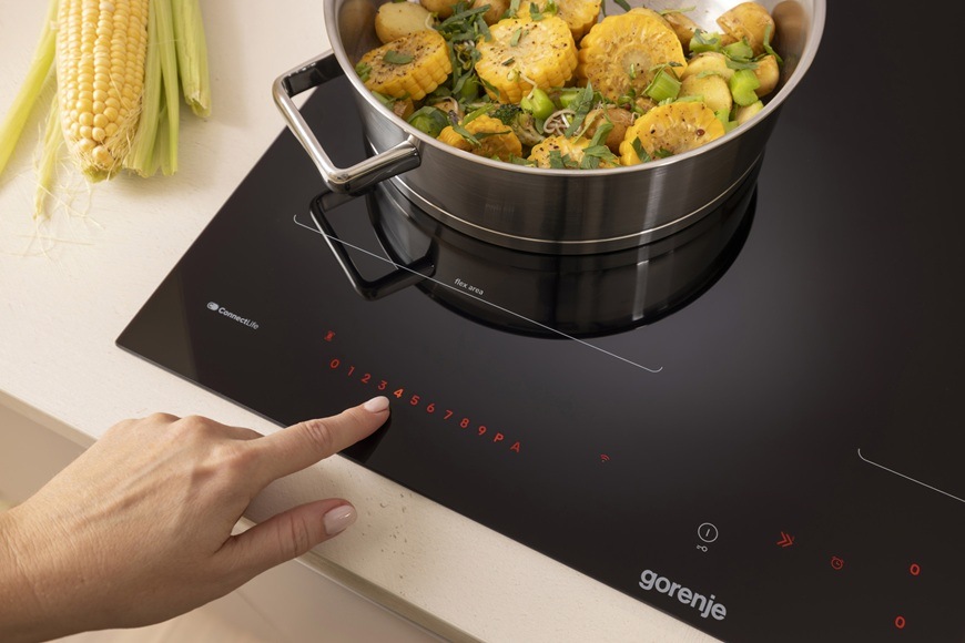 Na indukčnej varnej doske Gorenje GI6443BSCWF je položený hrniec av ňom sú nakrájané kukuricové struky a pór. Žena zvyšuje výkon varnej zóny.