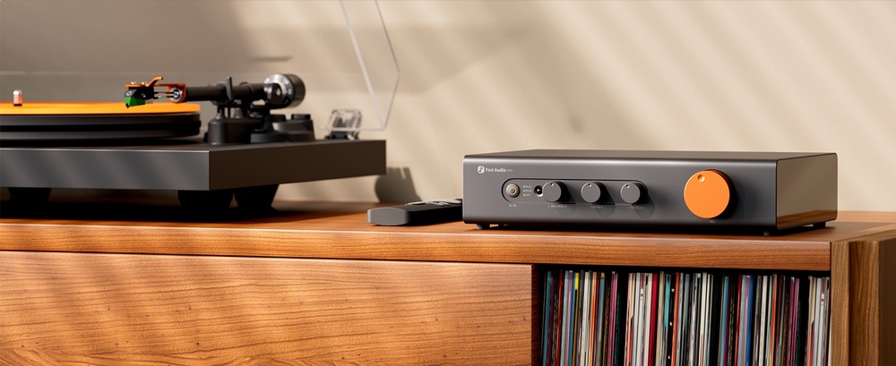 Zosilňovač Fosi Audio ZP3 čierny Predzosilňovač Fosi Audio ZP3 s výrazným oranžovým ovládačom stojí na drevenej skrinke vedľa gramofónu a diaľkového ovládača. V spodnej polici sú vinylové dosky.