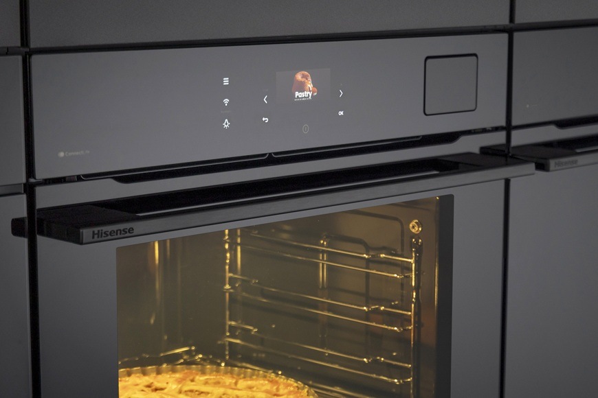 Detailný záber na ovládací panel pri vstavanej rúre Hisense BFS615S8B. Vnútri rúry sa pečie koláč.